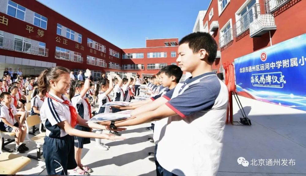 仪式上, 运河中学的 中学生手捧新校服,送到附属小学的小学生手中,并