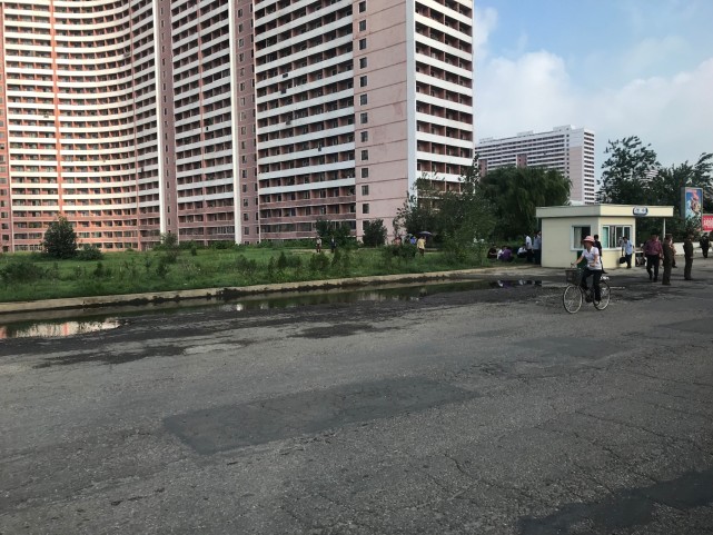 图为朝鲜平壤的马路,路上有积水,一名女子骑着自行车.