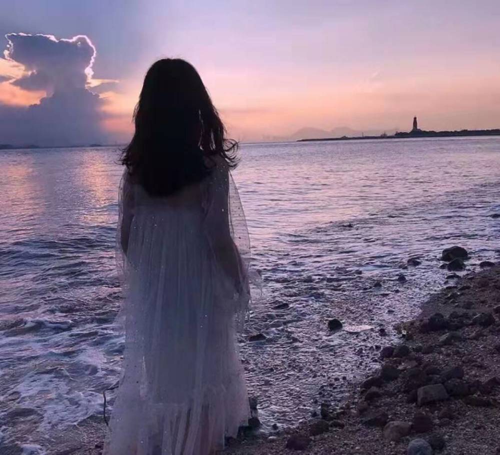 中的女生正在海边行走,大海真的能治愈人的心情,海上的夕阳虽然很冷的