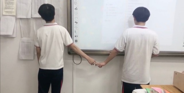 两个男同学吵架,被老师叫到讲台罚站,看着他们拉手的姿势,还真是有点