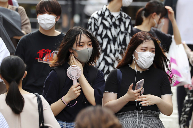 日本东京,高温已至,口罩还得戴着,女生手持小风扇为面部降温