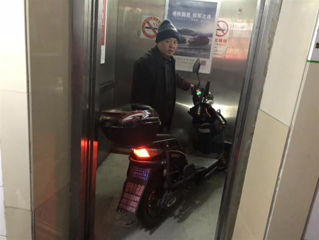 △东五小区居民董老伯正在向记者演示“梯控”的效果，电瓶车推入电梯后，电梯门顿时卡住。