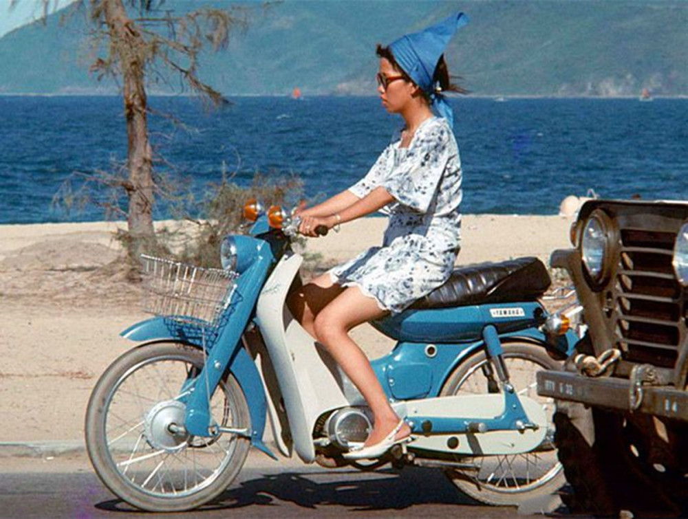 1960年代的越南芽庄,一个骑着摩托车的越南少女行驶在沿海滨的路上.