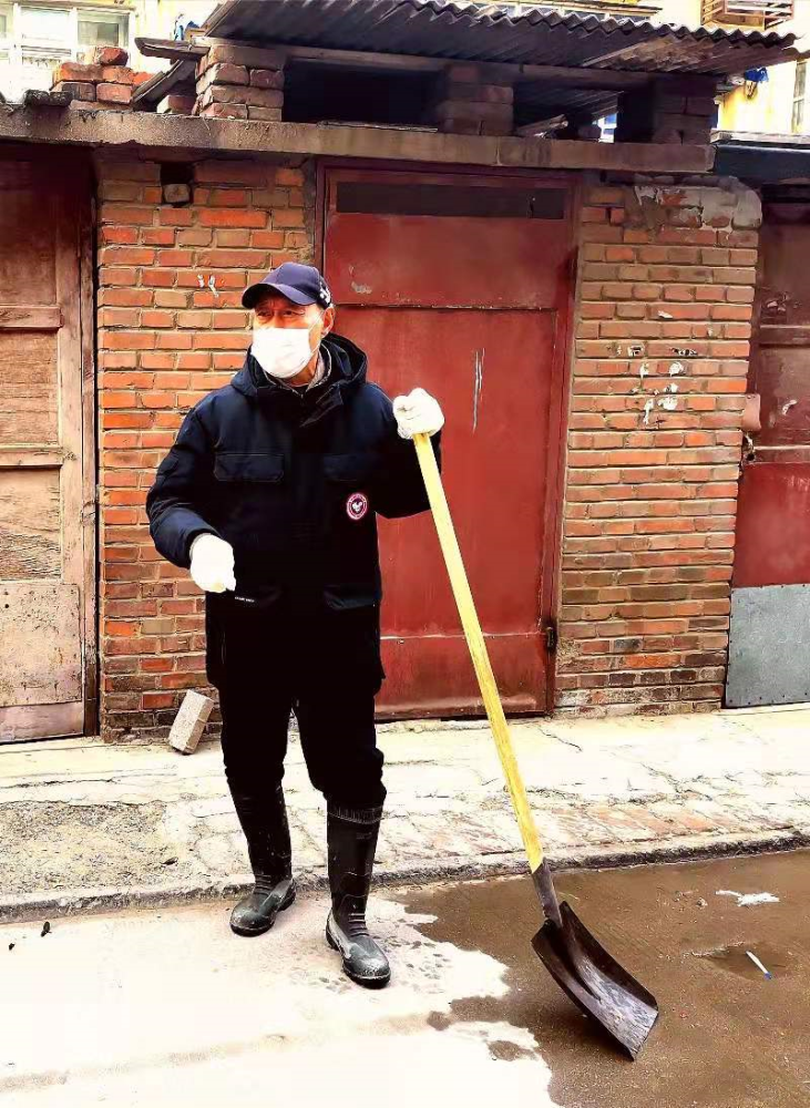 眼前的老人穿着及膝的雨靴, 拿着铁锹, 正在清理居民楼前外溢的污水.