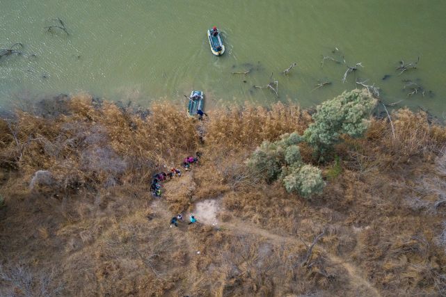 移民家庭和孩子爬上格兰德河的河岸进入美国,走私者乘坐皮筏从得州