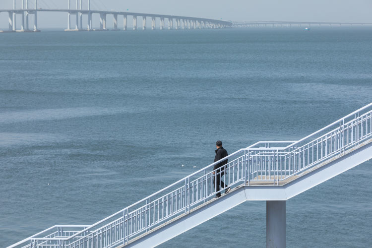 市民在环湾路海边的过街天桥上欣赏胶州湾风光.