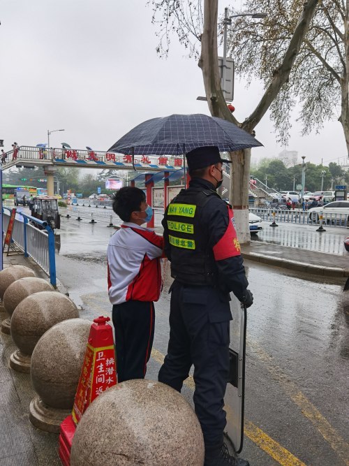 一名学生踮着脚尖将雨伞撑在了学校外执勤的特警队员的头顶.