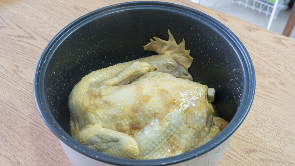 电饭煲内先放上土豆,再铺上葱段,姜片,最后把鸡放进来,腌制鸡的汤汁也