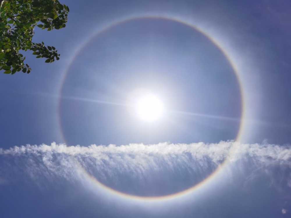 太阳被一道美丽的七色光圈彩带环绕,衬着淡蓝的天空,光圈内现出一层