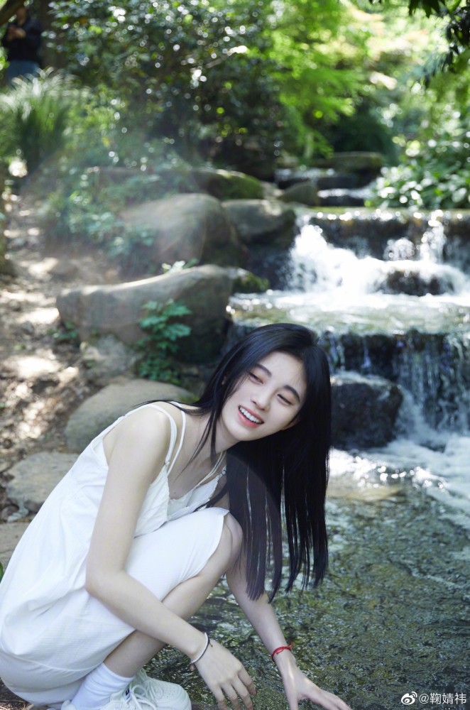 鞠婧祎身穿一袭白裙,在缓缓而流的小溪边上 站在岸上的石头边 阳光射