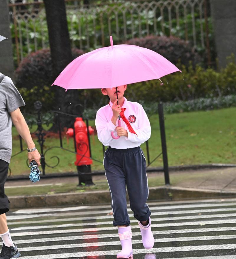 上学的孩子撑着伞,穿着雨靴.