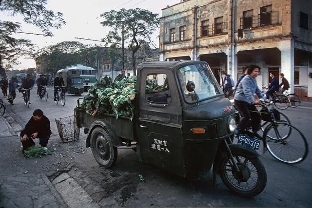 路边停着一辆卖菜的三轮车,那是60年代风靡中国的主力交通工具"东风