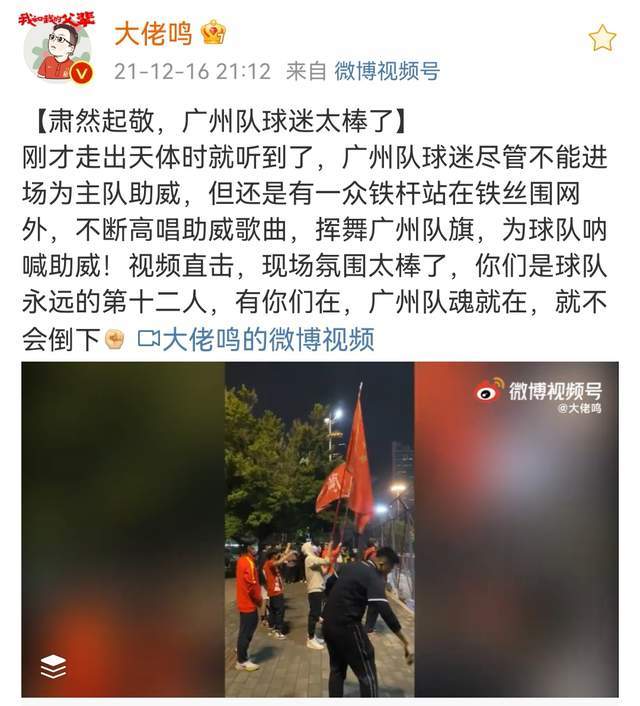 十几位广州队球迷在铁丝网外举着旗帜高唱歌曲路人一脸诧异