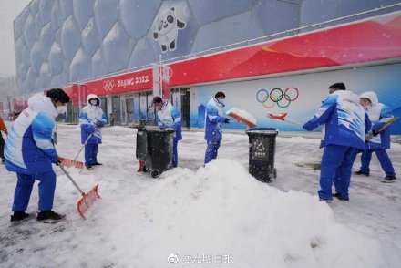 冬奥志愿者在冰立方前扫雪铲冰