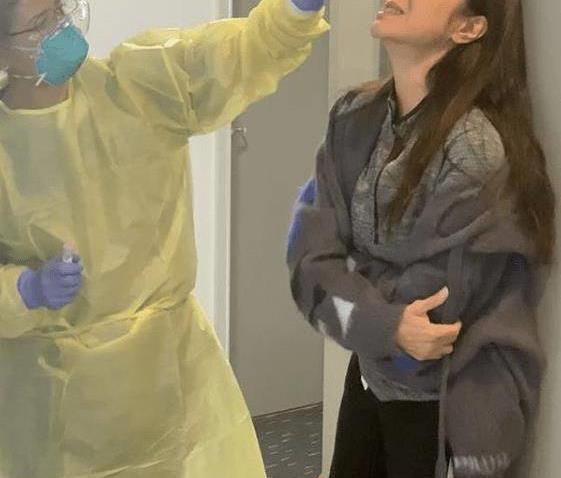 照片中的她在接受鼻腔拭子取样时紧闭双眼痛苦抱肘身体后缩紧贴墙壁