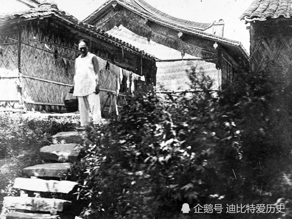 一名男子站在苇席搭成的房子旁边.