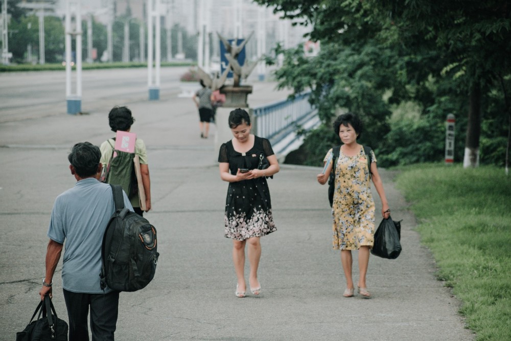 图为平壤街头步行的路人,一名女子边走路边低头看手机.