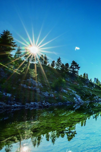 阳光透过小山坡直射湖面,湖水清澈见底.