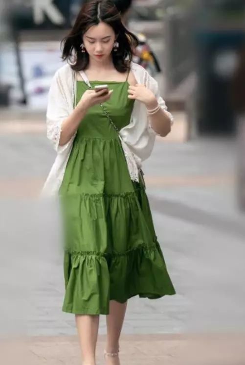 面容清丽的小姐姐,身穿一条绿色的吊带连衣裙,外搭件白色的开衫,走在