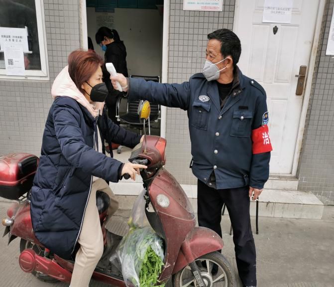 疫情防控安保人员对进入人员进行体温测量.