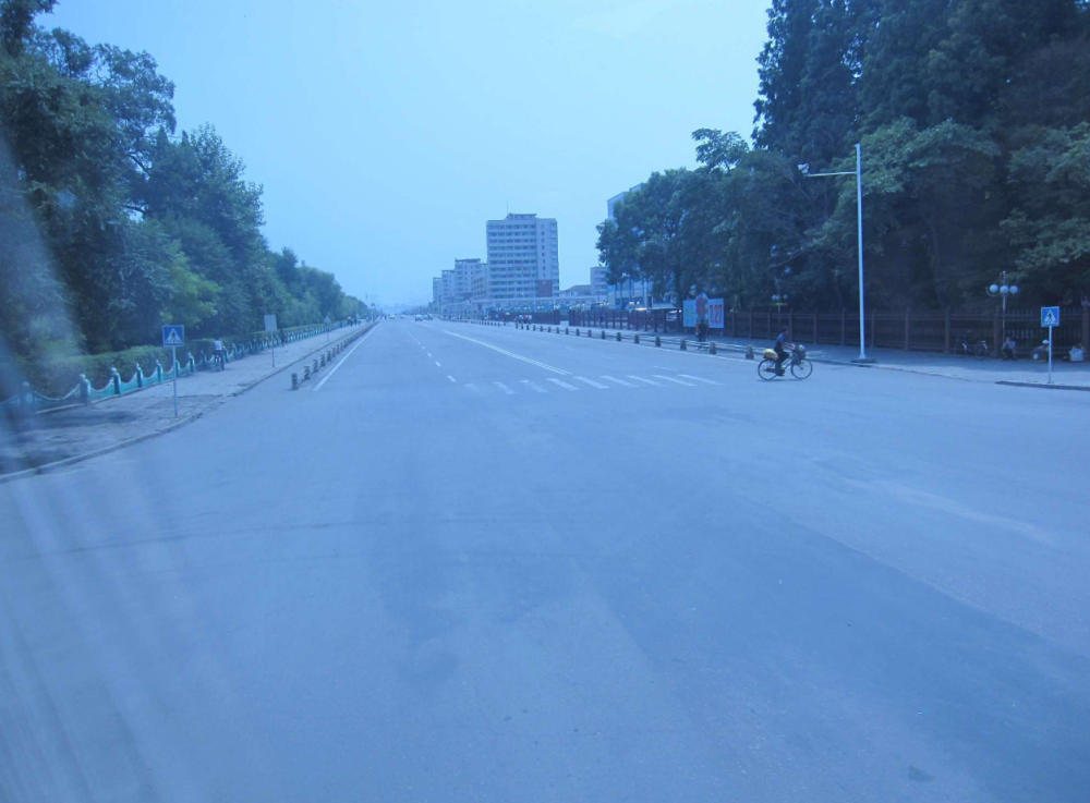 图为朝鲜第四大城市新义州街景,空旷的马路上汽车很少,一辆男子骑着