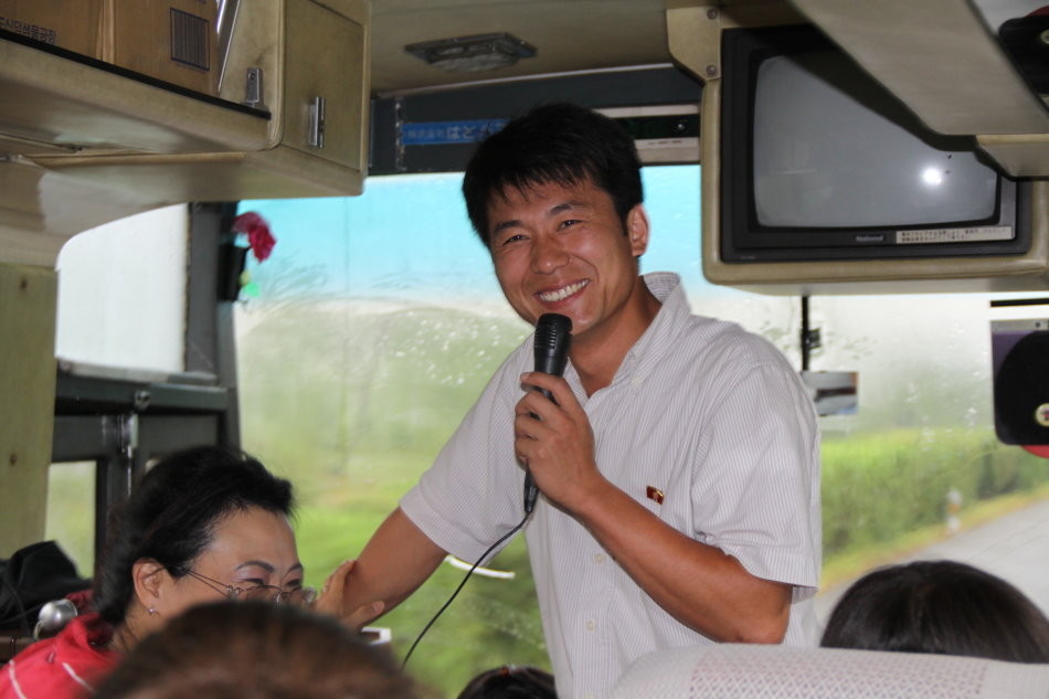 图为朝鲜一辆旅游大巴车上,一名男导游拿着话筒,笑得很开心.