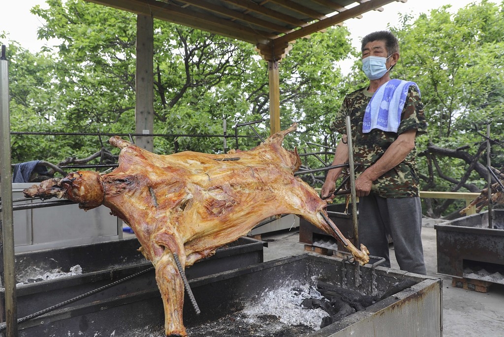 图为一名村民在为树上餐厅内就餐的游客制作烤全羊,香味四溢令人垂涎