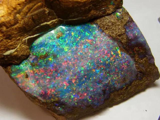 欧泊包裹在铁矿石的表面,让深色铁矿石的映衬使它的颜色看起来十分