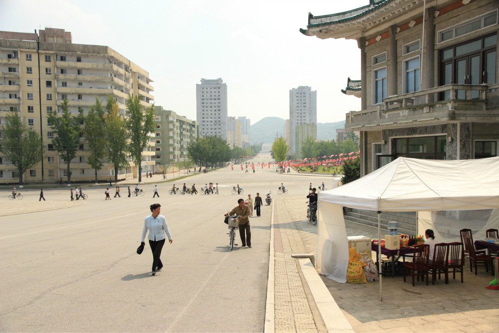 图为朝鲜开城街景,很多人推着自行车或步行过马路.