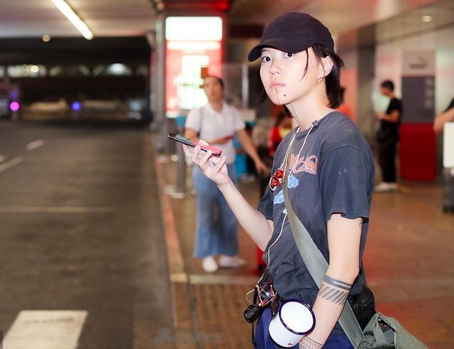 窦靖童现身机场，手臂“滚”字纹身吸睛，腰间搪瓷杯不离身