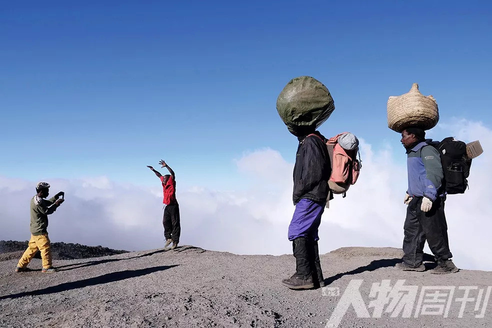 7月25日,挑夫们背着行李走在乞力马扎罗山登山道上,有两位挑夫休息时