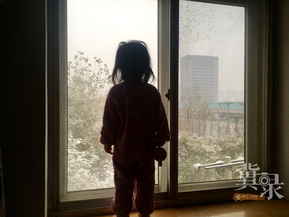 一位小朋友站在自家飘窗前,看着窗外雪花.