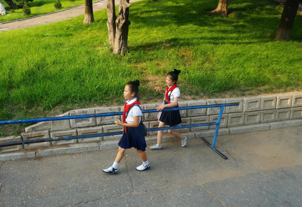 图为朝鲜平壤街头,两名穿着校服的小女孩一前一后走在路上.
