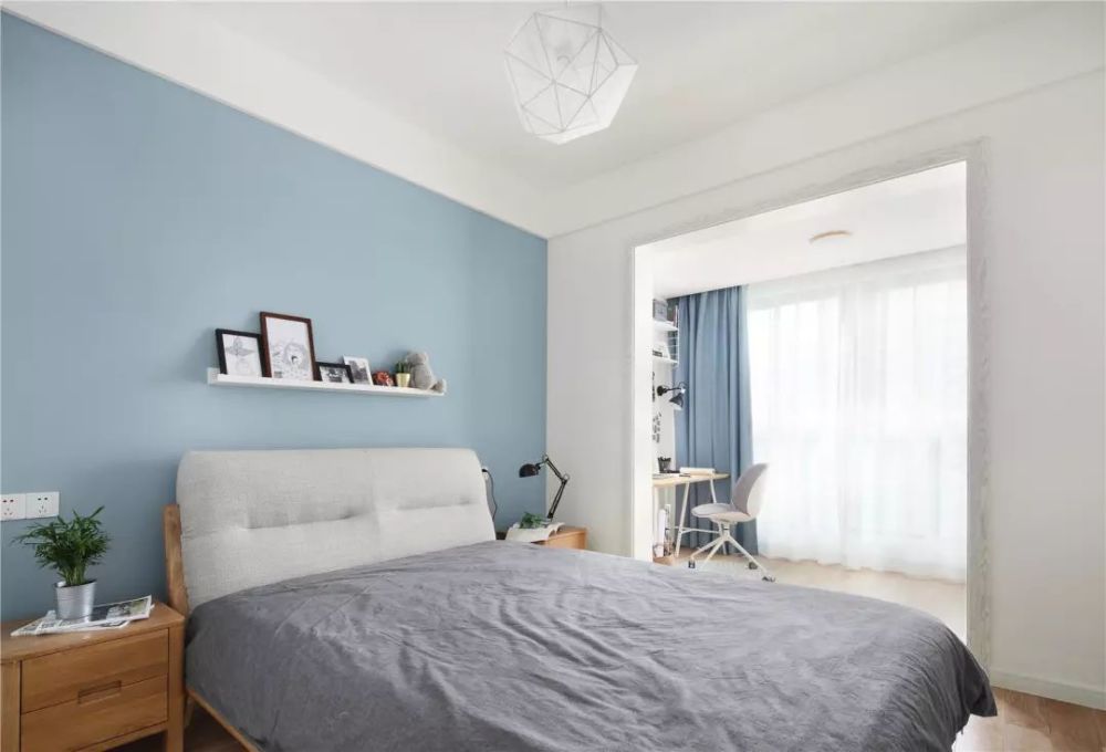 主卧摆放着一张木质床铺,床头背景用淡蓝色装饰,使整个空间营造出宁静