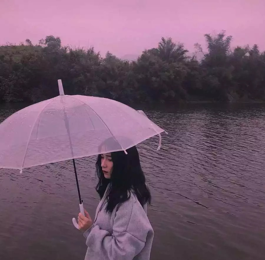 穿着灰色的上衣手里拿着一把透明的伞,站在湖边看着有一种伤感的感觉