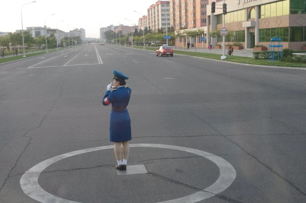 图为朝鲜平壤的马路上,一名女交警站在白色的圈圈内指挥交通.