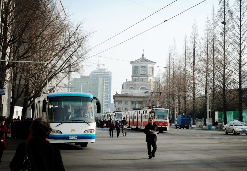 图为朝鲜平壤大街上,马路上有很多公交车和路人.