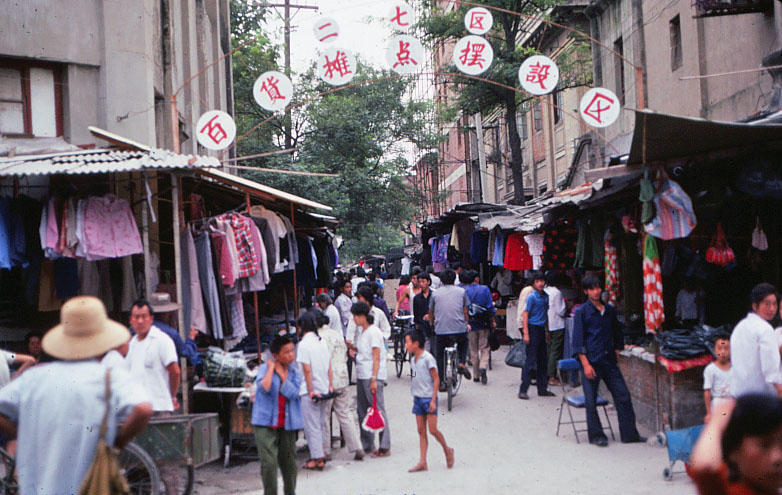 80年代郑州老照片:郑州市三七区百货摊点摆设区,街道两边是卖服装的