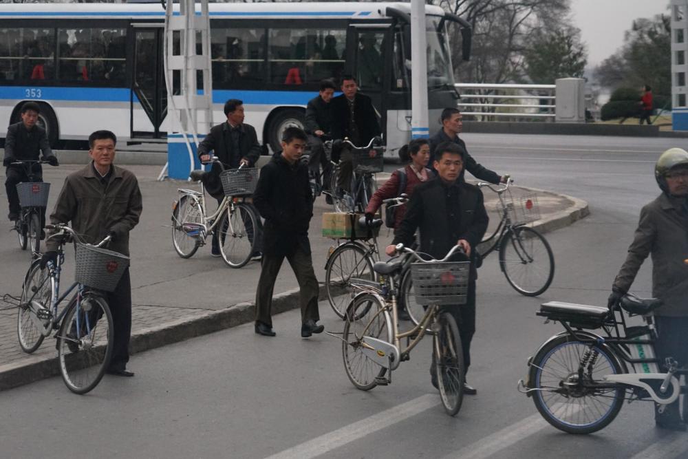 图为朝鲜平壤大街上推着自行车的市民,骑自行车出行是很多平壤市民的