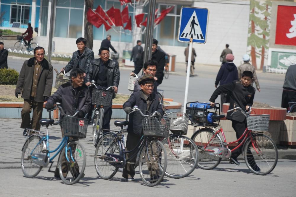 图为朝鲜街头出行的路人,很多人都推着或是骑着自行车.