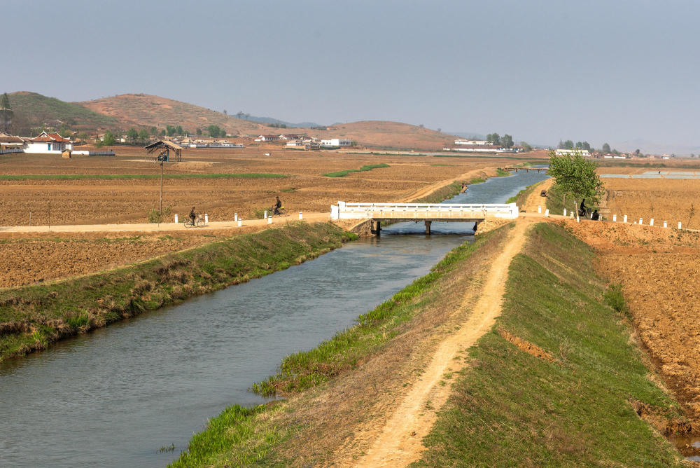 图为朝鲜农村地区的河流,河水非常清澈,旁边有两名男子骑着自行车.