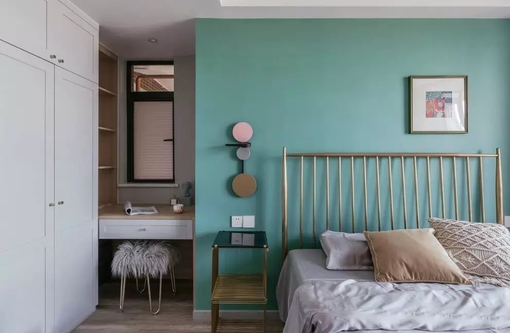 次卧里是刷了青色的墙壁,在床头位置有一个床头柜,在墙壁上面还可以挂