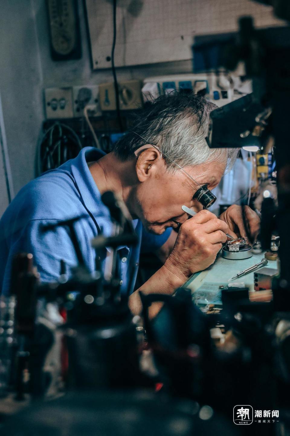 边,82岁的房锦章埋着头,用一枚戴在右眼的放大镜观察着已经拆开的手表