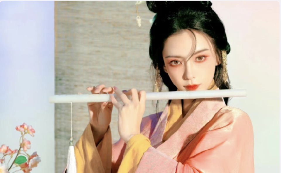 她两只手拿着笛子,大眼睛,烟熏妆,还是有古装美人的那个味儿.