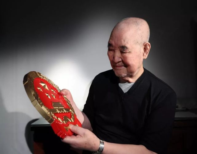 参与制造新中国第一枚金属国徽的吴嘉祜在家中观看金属国徽模型。图片来源：新华社