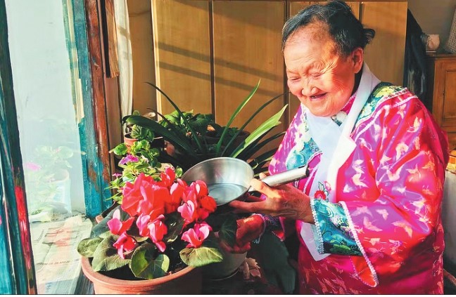 70岁的满族邵玉文老人穿着鲜艳的满族节日服装正在浇花.