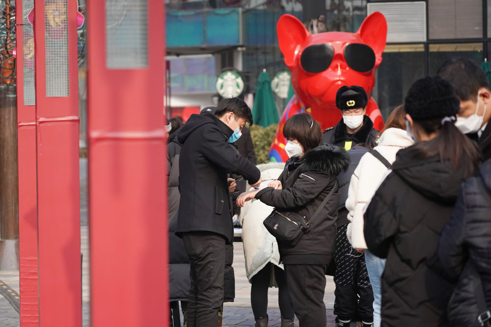 2月12日,在北京市朝阳区三里屯太古里,工作人员为进入商业区的人们