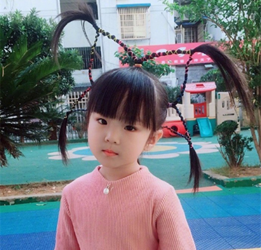 着一身粉色的连衣裙,脸颊两侧垂落着两根小辫儿,头顶上顶着两根冲天辫