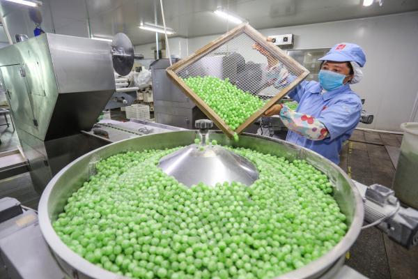 3月9日,福建晋江奇峰食品公司生产车间,工人在向包装机上倾倒糖果.