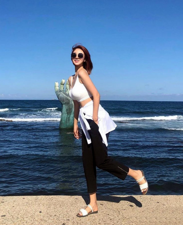女模特海边拍摄大片,穿白色背心搭黑裤简约休闲,戴墨镜可爱迷人